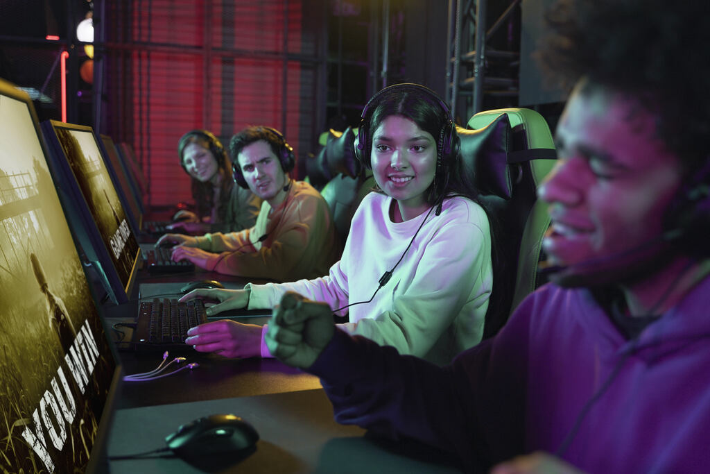  aposta no cblol: 4 dos 5 jogadores que disputam uma partida , sentados em suas cadeiras com braços apoiados na mesa que possuem seus mouses e teclados