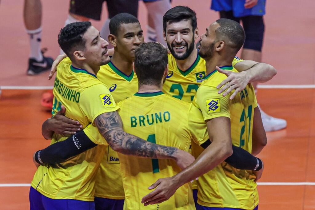 Jogadores da seleção brasileira de vôlei, abraçados em círculo, com uniforme amarelo, comemorando ponto na partida.