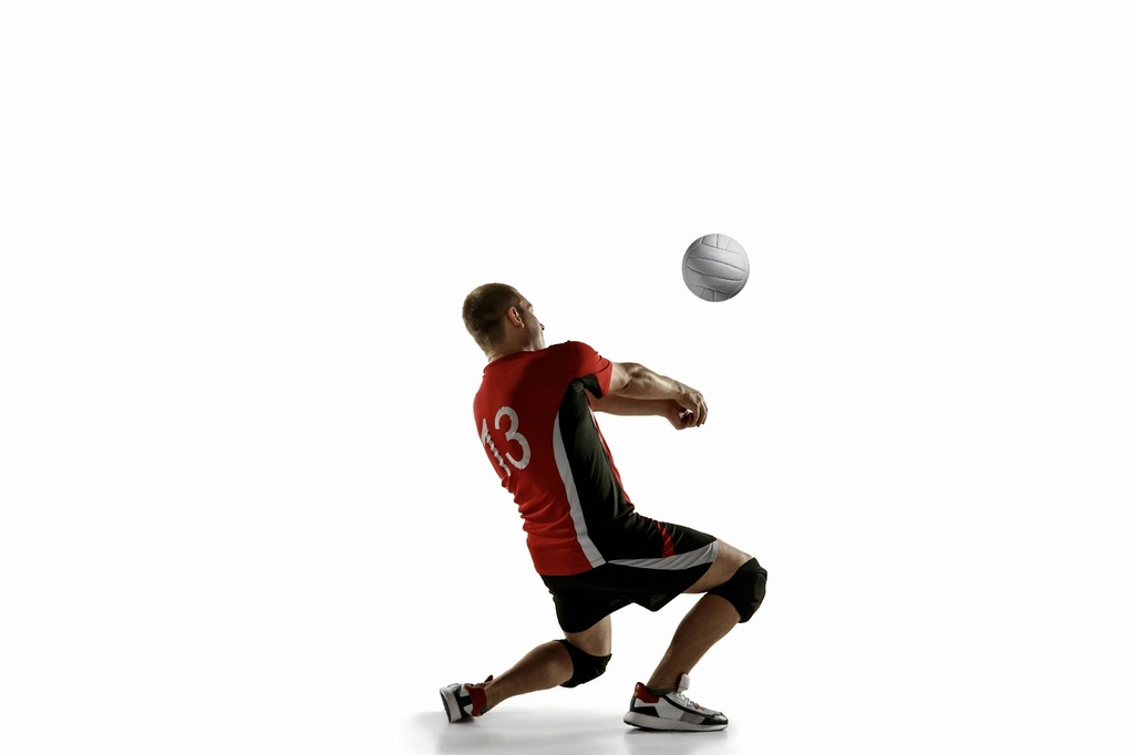 Jogador de camisa vermelha recepciona a bola de vôlei de um lançamento.