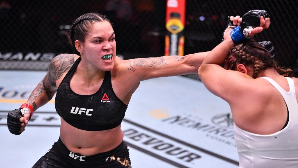 Lutadora Amanada Nunes acertando soco com a mão esquerda em lutadora adversária de roupa branca.