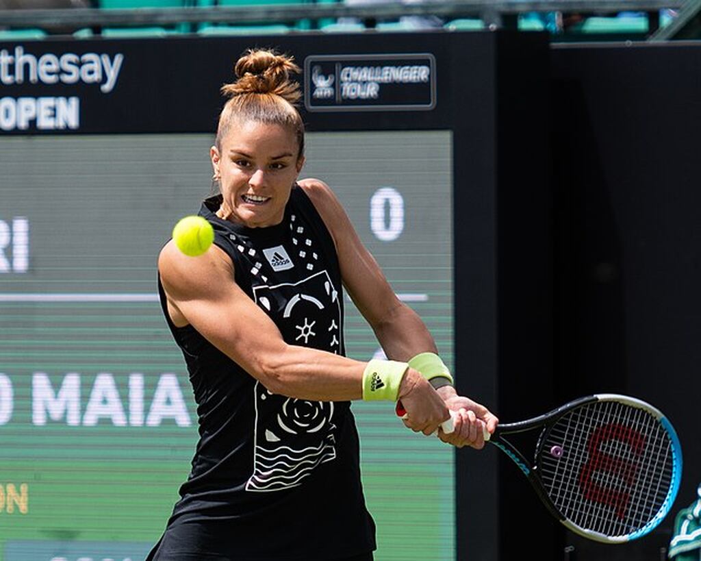 Jogadora de tênis Maria Sakkari, vestindo roupa preta e rebatendo a bola com raquete sendo segurada com as duas mãos.