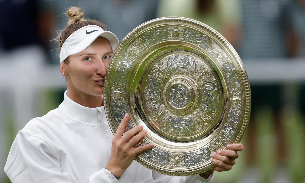 Jogadora de tênis, Marketa Vondrousova, vestindo roupa branca e beijando troféu redondo.