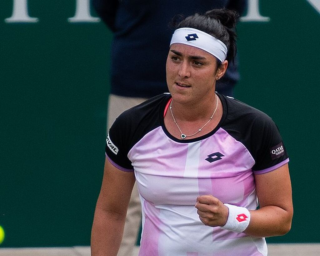 Jogadora de tênis Ons Jabeur, vestindo roupa rosa com detalhes pretos, comemorando ponto marcado durante partida.